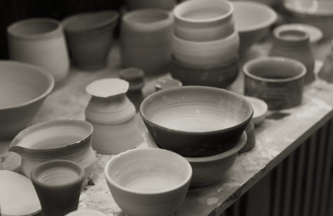 Glazed stoneware bowls and mugs arranged on a wooden shelf in a pottery studio