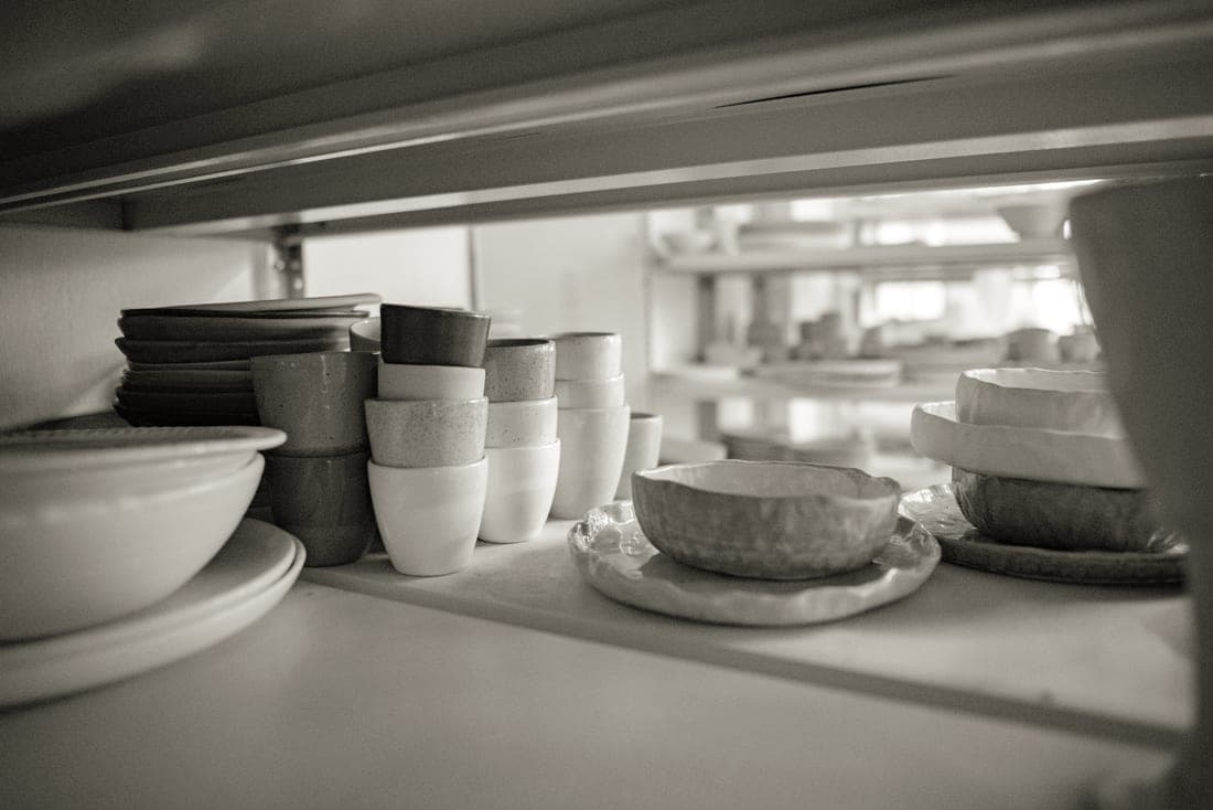 Stoneware mugs and bowls stacked on a kitchen shelf