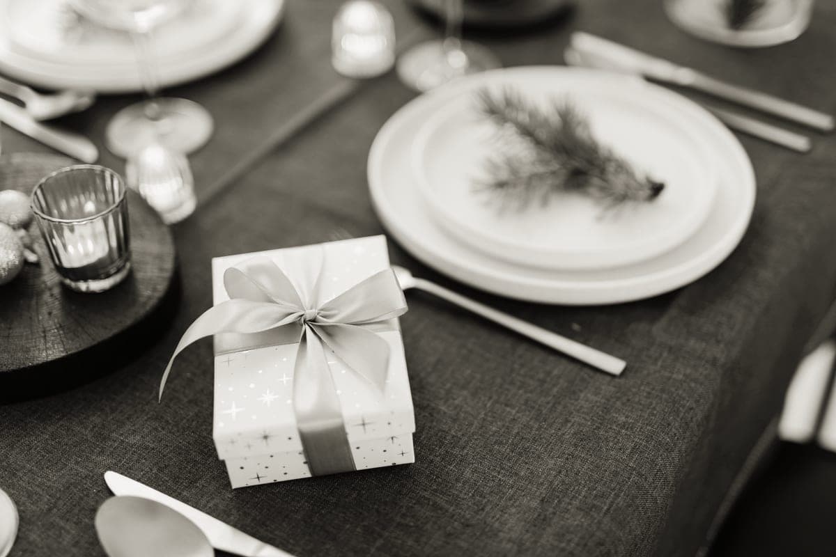 A wrapped gift box on a set dinner table with candles and greenery
